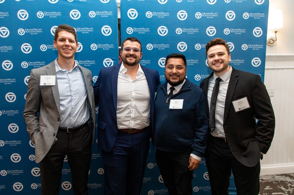 Alex Hogarth poses with 3 men in front of GVSU background